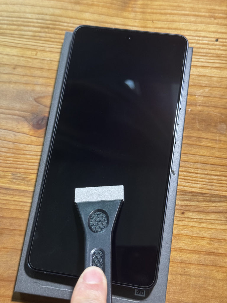 付属の専用ヘラでGalaxy S26 Ultraの画面から気泡を押し出している様子